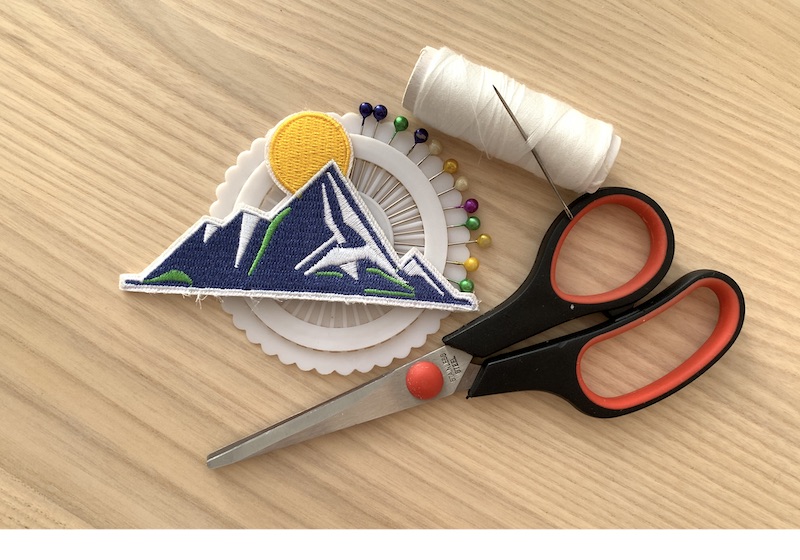 patch, sewing pins, white thread with needle and scissors on a wooden table