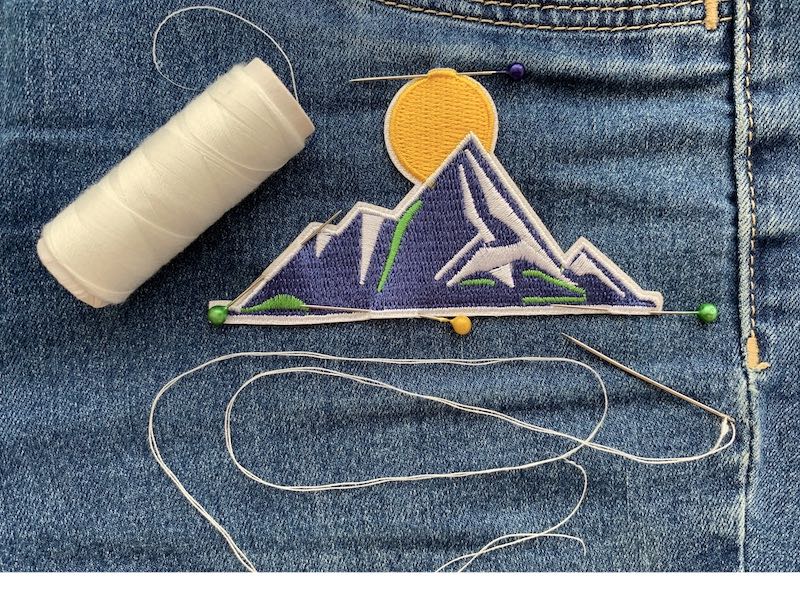 Patch pinned with denim fabric with white thread and a needle 