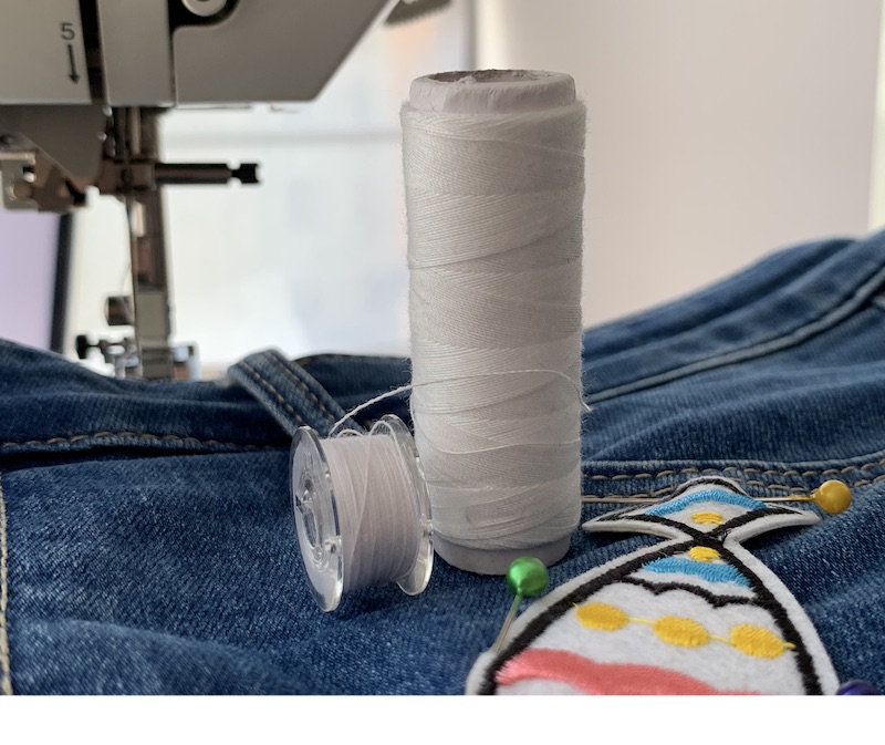 White thread and bobbin with white thread on a denim fabric