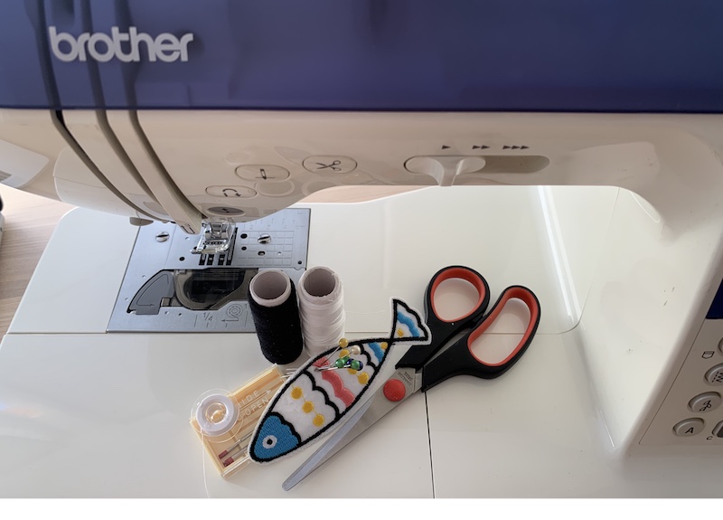 black and white thread, patch, scissors, bobbin, needles and sewing pins on a sewing machine