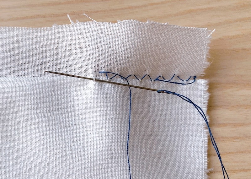 sewing a blind hem stitch by hand on a piece of white fabric