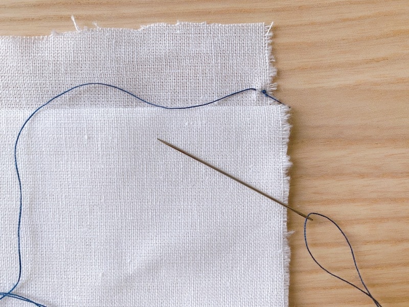 piece of white fabric with a blue thread stitch with a knot at the end