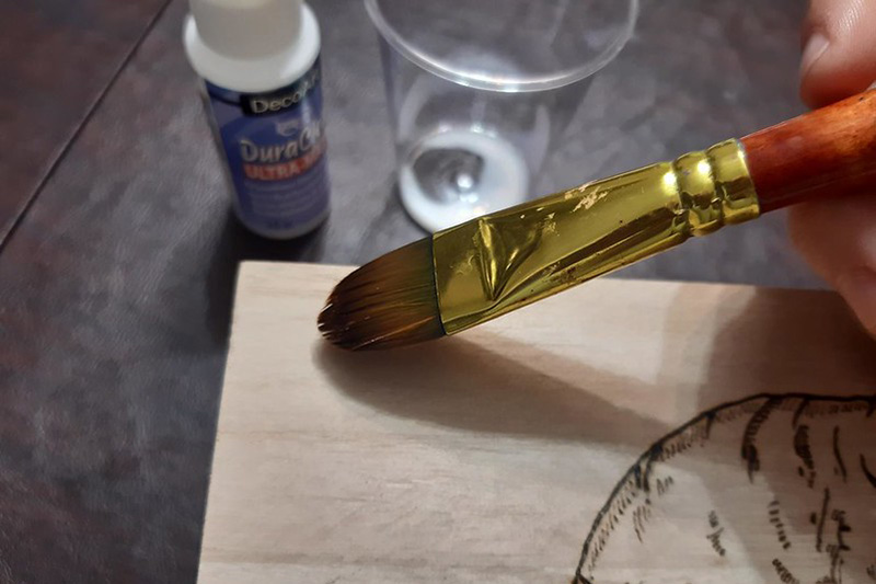 a person applying a coat of varnish onto a pyrography project